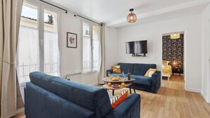 A modern living room with a blue sofa, a coffee table with drinks, and a TV mounted on the wall. - 865 Suite Jasmin - Superb apartment (Montreuil)