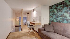 A modern living room with a grey sofa, a wooden desk, and a chair. There is a patterned wallpaper on the wall and a wooden floor. - 194 Suite Parisian house (Paris)