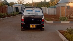 Un coche Chevrolet negro estacionado en una zona rural con un cartel en la parte trasera que dice 'Dunduzu Village'.
