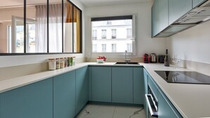 A modern kitchen with teal cabinetry, a window with curtains, a sink, and a stove. - 675 Suite Bolivar - Superb apartment in Paris (Paris 19 Buttes-Chaumont)