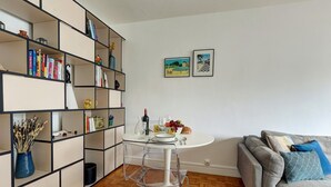 A modern living room with a white round table, clear glass chairs, a grey sofa, and a bookshelf filled with books and decorative items. - 675 Suite Bolivar - Superb apartment in Paris (Paris 19 Buttes-Chaumont)