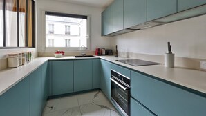 A modern kitchen with teal cabinetry, a large window, and a marble floor. - 675 Suite Bolivar - Superb apartment in Paris (Paris 19 Buttes-Chaumont)