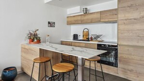 A modern kitchen with a marble countertop, wooden cabinets, and a built-in stove. There are three stools and a potted plant on the counter. - 620 Suite Martel - Superb apartment in Paris. (Paris 10 Entrepôt)