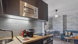 A modern kitchen with a built-in microwave, a coffee maker, and a dishwasher. There is a dining area with a table and chairs, and a sofa in the background. - 867-Suite Mimosa - Superb Apartment (Montreuil)