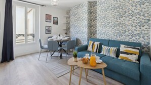 A modern living room with a blue sofa, a dining table with chairs, and a patterned wall. - 867-Suite Mimosa - Superb Apartment (Montreuil)