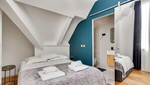A modern bedroom with a sloped ceiling, a bed with white linens, a small bedside table, and a bathroom visible through an open door. - 240 Suite Elysée - Superb apartment in Paris (Paris 08 Élysée)