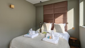 A neatly made bed with white linens, a brown headboard, and a bedside table with a bottle and glasses. - 365 Suite Fondary 4 - Superb apartment in Paris (Paris 15 Vaugirard)