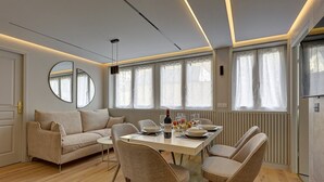 A modern living room with a sofa, dining table, and chairs. There is a large mirror on the wall, and the room has large windows with curtains. - 365 Suite Fondary 4 - Superb apartment in Paris (Paris 15 Vaugirard)