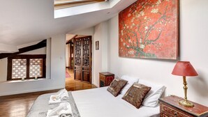A bedroom with a bed, a red lamp, a painting, and a view of a wooden floor and a door. - 2•5•9 Suite Suzy • Cosy Duplex • Paris (Paris 11 Popincourt)