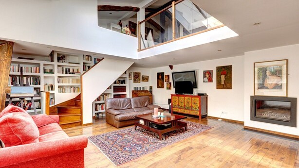 A spacious loft with a high ceiling, a staircase, a living room with a sofa, a coffee table, and a fireplace. - 2•5•9 Suite Suzy • Cosy Duplex • Paris (Paris 11 Popincourt)