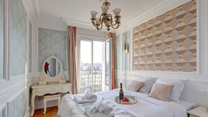 A hotel room with a large bed, a vanity with a mirror, a chandelier, and a geometric-patterned wall.