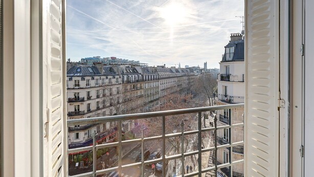 A view from a balcony overlooking a row of Parisian buildings with a clear sky and the sun shining.