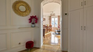 A hallway with a red chair, a gold mirror, and a dining area with a chandelier.