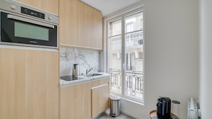 Et moderne køkken med træskabe, en indbygget ovn, en marmor bordplade, en vask og et vindue med udsigt til en balkon.