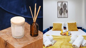 Ein Zimmer mit einem Bett, einem Gemälde und einem Holztisch mit Kerze und Reed-Diffuser.