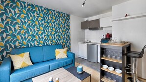 Ein kompakter Wohnbereich mit einem blauen Sofa, einem Couchtisch, einer Küchenzeile mit Spüle und Schränken sowie einer Wand mit Muster.