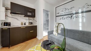 Een moderne keuken met donkere kastjes, een marmeren spatwand en een zwart aanrecht. Er staat een grijze bank met een witte orchideeplant ernaast.