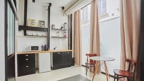 A compact kitchen with a microwave, cabinets, and a small dining table with chairs. - 294 Suite Naza - Superb apartment in Paris (Paris 03 Temple)