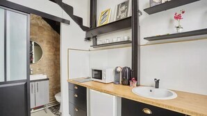A modern bathroom with a wooden countertop, a white sink, and a black and white cabinet. There are shelves above the sink with decorative items and a small potted plant. - 294 Suite Naza - Superb apartment in Paris (Paris 03 Temple)