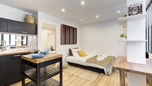 A compact hotel room with a kitchenette, a bed with a yellow pillow, a small bedside table, and a window with a view. - 318 Suite Pivert - Superb apartment in Paris (Paris 11 Popincourt)