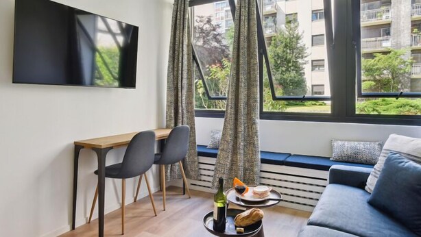 A modern living room with a wooden desk, two chairs, a sofa, and a dining table with a bottle of wine and bread. - 313 Suite Lemon - Superb apartment in Paris (Paris 12 Reuilly)