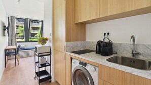 A compact kitchen with a washing machine, a sink, and a small dining area with a chair and table. - 313 Suite Lemon - Superb apartment in Paris (Paris 12 Reuilly)