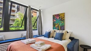 A hotel room with a bed, a window with curtains, a painting on the wall, and a view of greenery outside. - 313 Suite Lemon - Superb apartment in Paris (Paris 12 Reuilly)