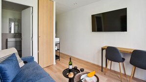 A modern living room with a blue sofa, a dining table with chairs, a flat-screen TV mounted on the wall, and a small side table with a bottle and glasses. - 313 Suite Lemon - Superb apartment in Paris (Paris 12 Reuilly)