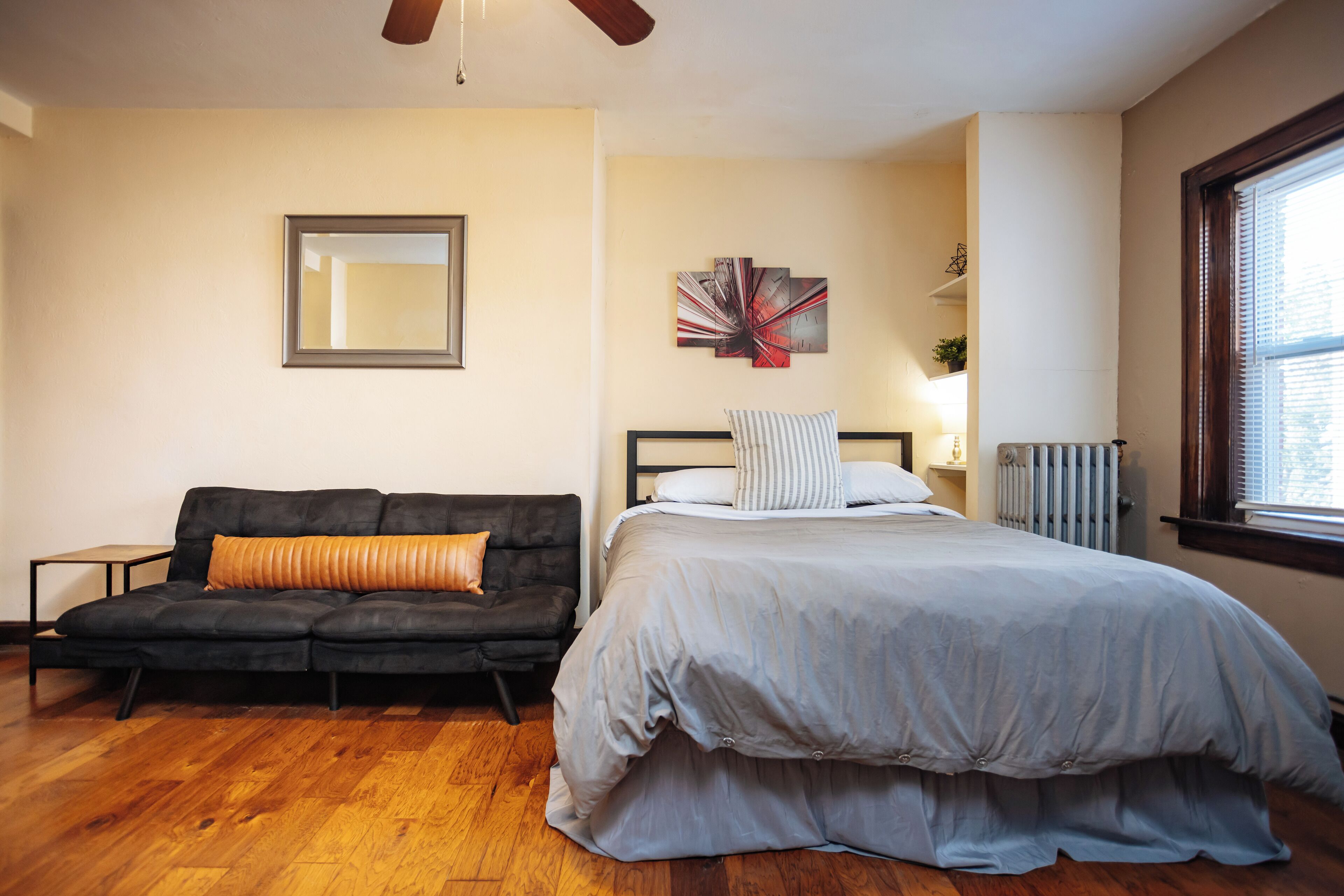 A bedroom with a bed, a black sofa, a mirror, and a radiator.
