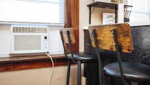 Une pièce avec un radiateur, deux chaises en bois, une étagère avec une plante en pot et une pancarte sur laquelle on peut lire : « Chez soi, on est bien ».