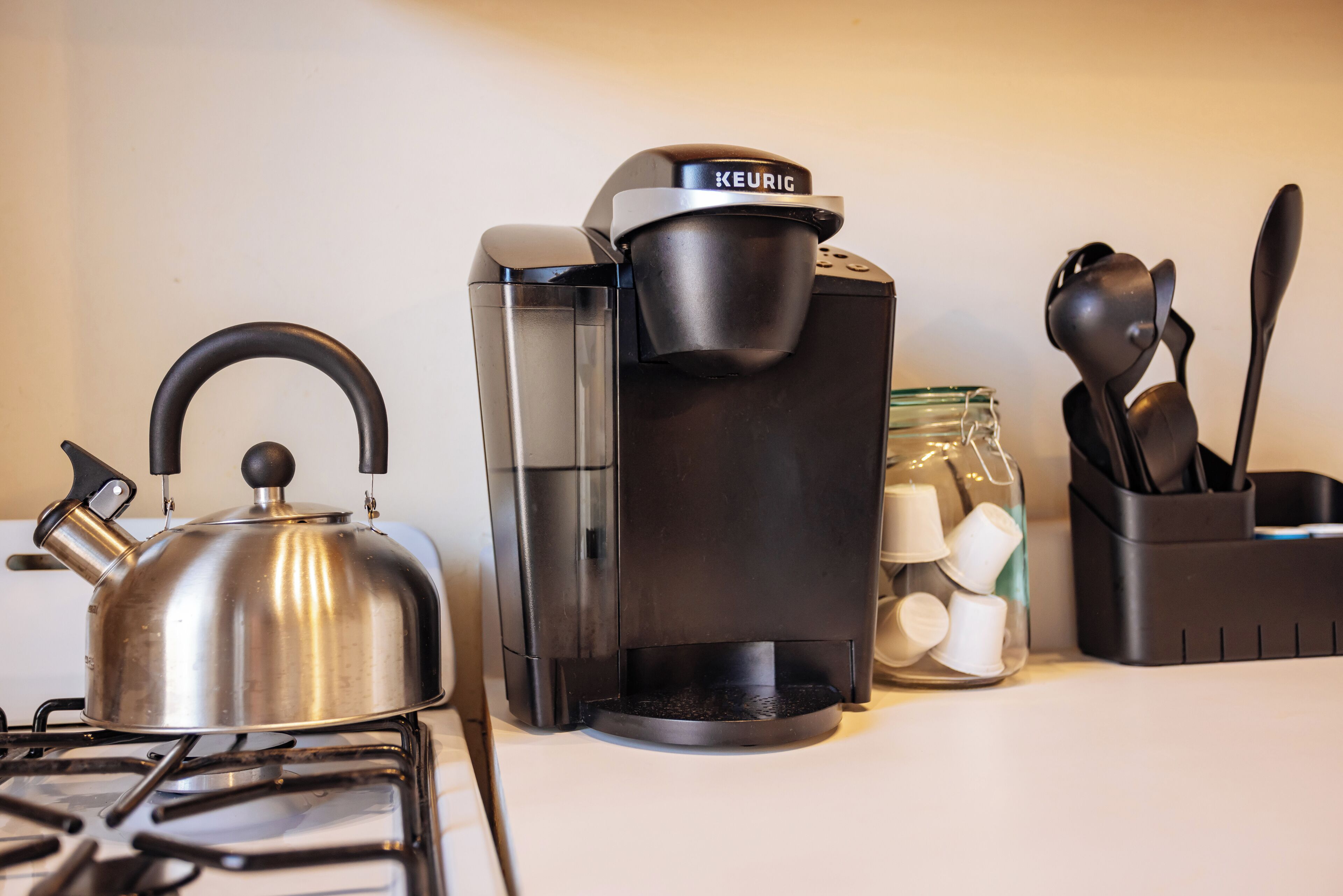 A kitchen with a kettle, a coffee maker, and a jar of tea bags.