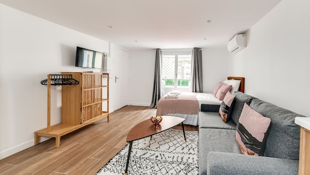 A modern, well-lit room with a bed, a sofa, a wooden wardrobe, and a television. - 136 Suite Harold - Superb apartment in Paris. (Paris 02 Bourse)