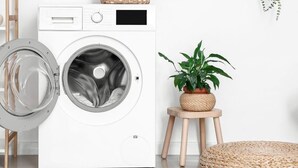 A modern laundry room with a front-loading washing machine, a small wooden stool, and a potted plant. - 369 Suite Fondary 5 - Superb apartment in Paris (Paris 15 Vaugirard)