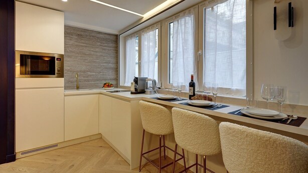 A modern kitchen with a built-in microwave, a coffee machine, and a dining area with bar stools and a window with curtains. - 369 Suite Fondary 5 - Superb apartment in Paris (Paris 15 Vaugirard)