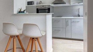 A modern kitchen with white cabinets, a microwave, and a stove. There are two wooden stools with metal rings. - 338 Suite Montmartre - Superb apartment in Paris (Paris 09 Opéra)