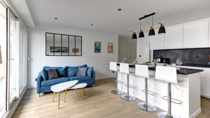A modern kitchen with white cabinets, a blue sofa, and a bar area with white chairs. - 320 Dolce Vita Suite - Superb apartment (Suresnes)