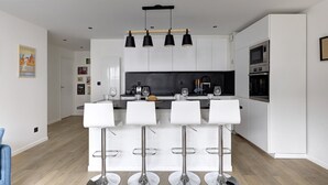 A modern kitchen with white cabinets, a black countertop, and four white bar stools. - 320 Dolce Vita Suite - Superb apartment (Suresnes)