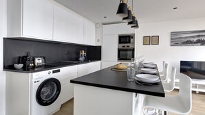 A modern kitchen with a washing machine, a microwave, and a dining area with a table set for four. - 320 Dolce Vita Suite - Superb apartment (Suresnes)