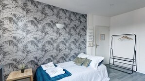 Un dormitorio con cama, mesita de noche, perchero y un papel tapiz estampado.