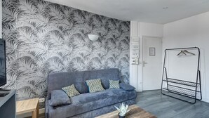 Una sala moderna con un sofá gris, papel tapiz estampado, una mesa de centro de madera y un tendedero de metal.