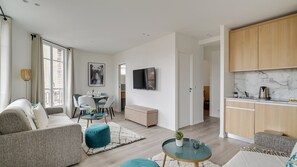 A modern living room with a sofa, a dining table with chairs, a TV mounted on the wall, and a kitchen area with wooden cabinets and a marble countertop. - 155 Suite Georges - Superb apartment in Paris (Paris 13 Gobelins)
