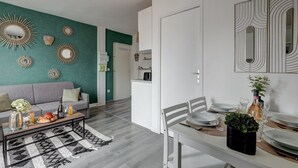 Ein modernes Wohnzimmer mit einem grauen Sofa, einem Couchtisch mit Getränken und Snacks sowie einem Essbereich mit einem weißen Tisch, gedeckt für zwei Personen.
