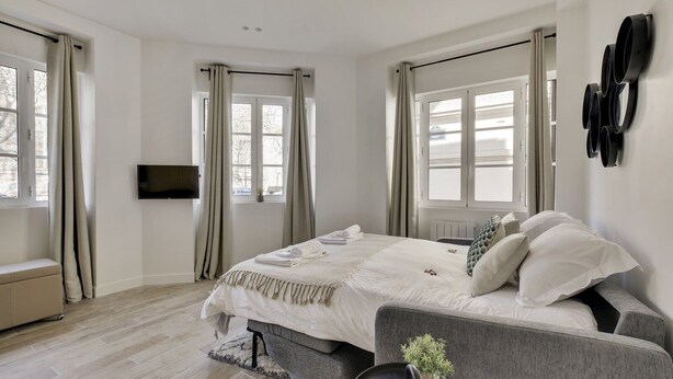 A modern bedroom with a large bed, a flat-screen TV, and a view of the outside through large windows. - 151 Suite Jean Yves - Superb Studio in Paris (Paris 13 Gobelins)