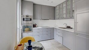 A compact kitchen with grey cabinets, a built-in oven, a sink, and a dining area with a table and chairs. - 629 Suite Damremont - Superb apartment in Paris (Paris 18 Buttes-Montmartre)
