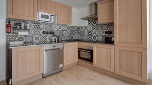 Eine Küche mit Holzausstattung, einer Mikrowelle, einem Geschirrspüler, einem Backofen und einer fliesenverzierten Spritzschutzwand.