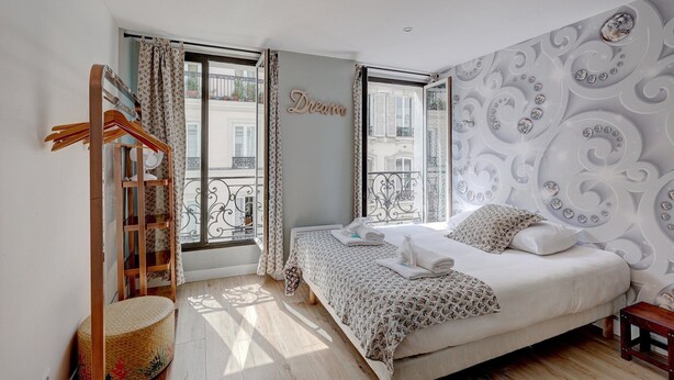 Ein Schlafzimmer mit Bett, Kleiderschrank, einem Fenster mit Vorhängen und einem Balkon.