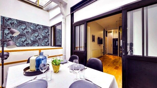 A dining area with a table set for four, a large window with a tropical leaf pattern, and a view into another room. - 113 Suite Lui - Sumptuous apartment in Paris (Paris)