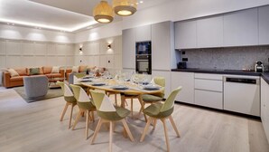 Eine moderne Küche mit weißen Schränken, ein Essbereich mit einem Holztisch und Stühlen sowie ein Wohnzimmer mit einer Couch und Kissen.