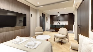 A modern hotel room with a bed, two armchairs, a small round table, a TV, and a kitchenette in the background. - 327 Suite Le Marais - Superb apartment in Paris (Paris 03 Temple)