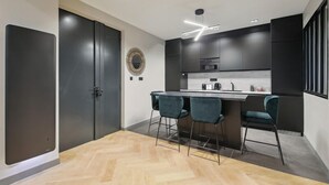 A modern kitchen with dark cabinetry, a central island with bar stools, and a herringbone wood floor. - 327 Suite Le Marais - Superb apartment in Paris (Paris 03 Temple)